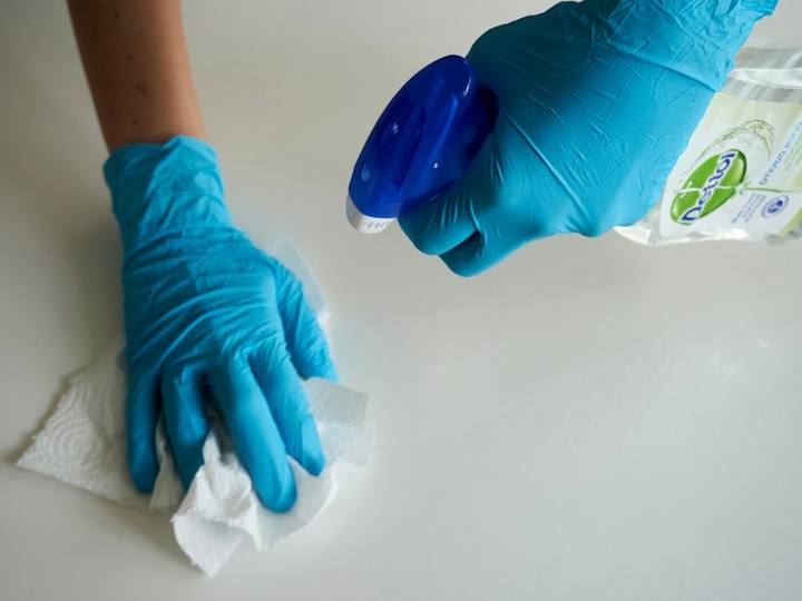 Gloved hands wiping a white surface with spray cleaner